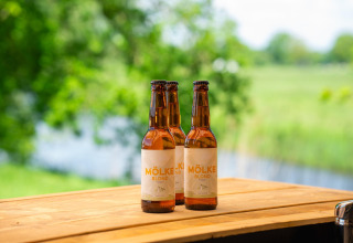 Trois bouteilles de bière Mölke Blond sur une table en bois dans la verdure à Holiday Park Mölke, Pays-Bas.