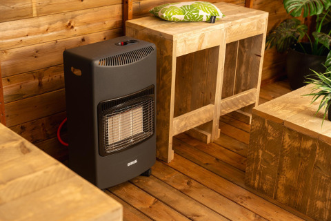 Inside a treehouse tent with a black gas heater, wooden furniture, and plants at Holiday Park Mölke, Netherlands.