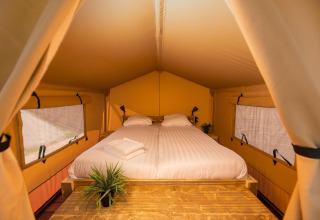 Interior of the Treehouse safari tent with a double bed and plants at Holiday Park Mölke in the Netherlands.