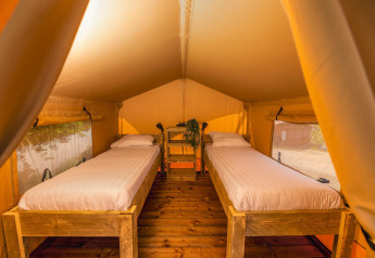 Interior de tienda safari con dos camas individuales en Holiday Park Mölke, Países Bajos, iluminación cálida.