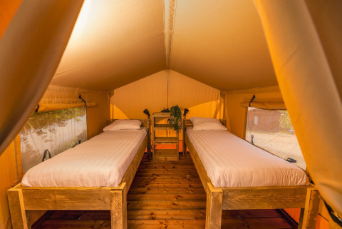 Interior de tienda safari con dos camas individuales en Holiday Park Mölke, Países Bajos, iluminación cálida.