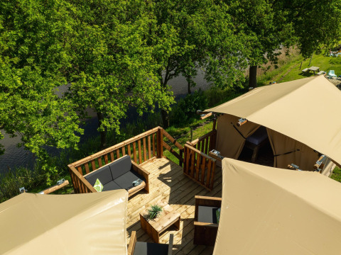 Boomhut safaritent bij Holiday Park Mölke in Nederland, met gezellig terras aan het water tussen bomen.