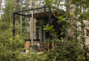 Sweet Cabin tiny house with outdoor hot tub nestled in the woods, surrounded by lush green forest.