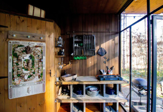 Knusse tiny house keuken met houten wanden, keukengerei en uitzicht op het bos buiten.