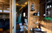 Knusse tiny house met keukenhoek, stapelbed, badkamer en sfeervolle lichtjes aan het plafond.