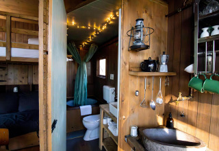 Knusse tiny house met keukenhoek, stapelbed, badkamer en sfeervolle lichtjes aan het plafond.
