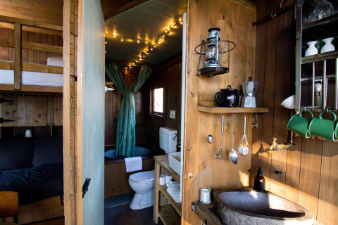 Gemütliches Tiny House mit Küche, Etagenbett, Bad, Hängelampe und Lichterketten im Innenraum.