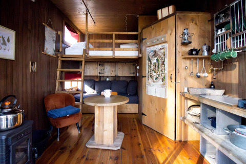 Gezellige tiny house met verhoogd bed, houten interieur, compacte keuken en knusse zithoek.
