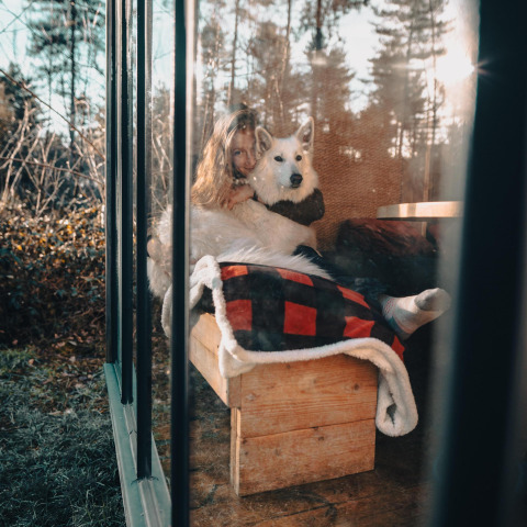 Mujer abraza a su perro blanco en el interior de una cabaña acogedora con grandes ventanales en Limburg, Bélgica.