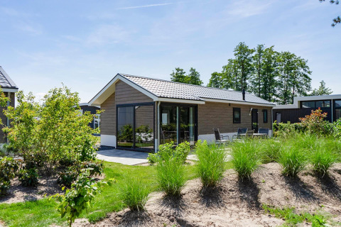 Moderne Velthorst lodge bij EuroParcs Veluwemeer, Nederland, met veel groen en buitenterras in de zon.