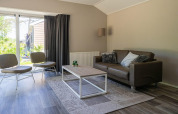 Sala de estar con sofá, sillas y mesa baja en una cabaña Velthorst de EuroParcs Veluwemeer, Países Bajos.