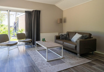 Sala de estar con sofá, sillas y mesa baja en una cabaña Velthorst de EuroParcs Veluwemeer, Países Bajos.