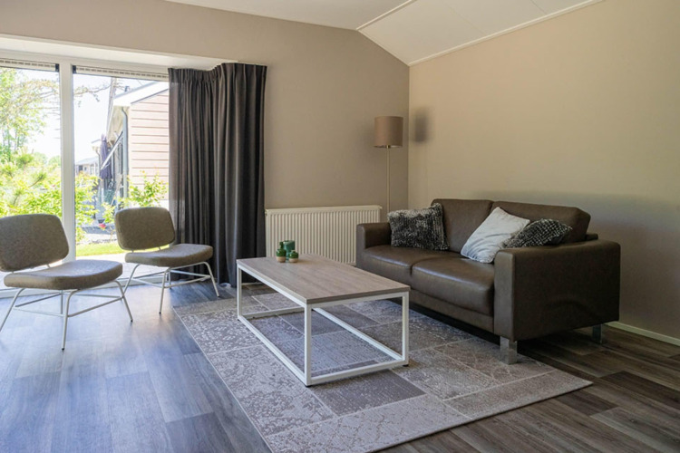 Sala de estar con sofá, sillas y mesa baja en una cabaña Velthorst de EuroParcs Veluwemeer, Países Bajos.