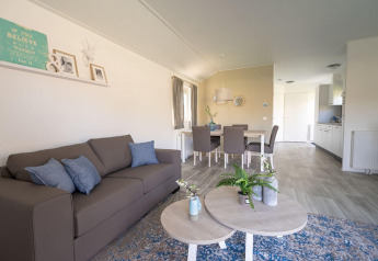 Helles und modernes Wohnzimmer der Velthorst-Lodge im EuroParcs Veluwemeer, Niederlande, mit Sofa und Esstisch.