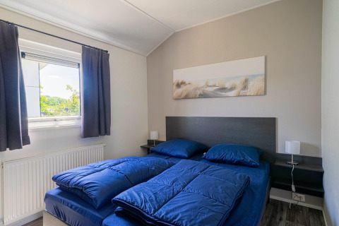 Slaapkamer in Velthorst lodge bij EuroParcs Veluwemeer met blauw beddengoed en een wanddecoratie.