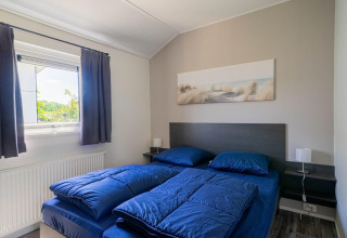 Slaapkamer in Velthorst lodge bij EuroParcs Veluwemeer met blauw beddengoed en een wanddecoratie.