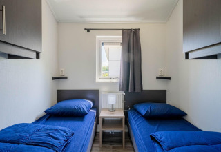 Dormitorio moderno y compacto con dos camas individuales y ropa de cama azul en Velthorst lodge, EuroParcs Veluwemeer.