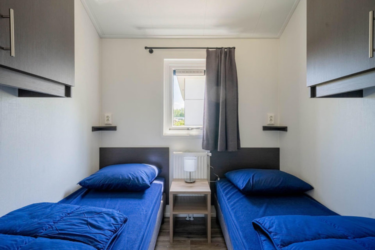 Dormitorio moderno y compacto con dos camas individuales y ropa de cama azul en Velthorst lodge, EuroParcs Veluwemeer.