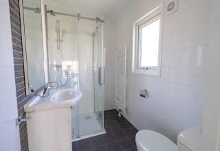 Moderne badkamer bij Velthorst-lodge, EuroParcs Veluwemeer, met glazen douche, wastafel en raam.