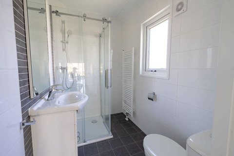 Baño moderno en la cabaña Velthorst de EuroParcs Veluwemeer, con ducha de cristal, lavabo y ventana.