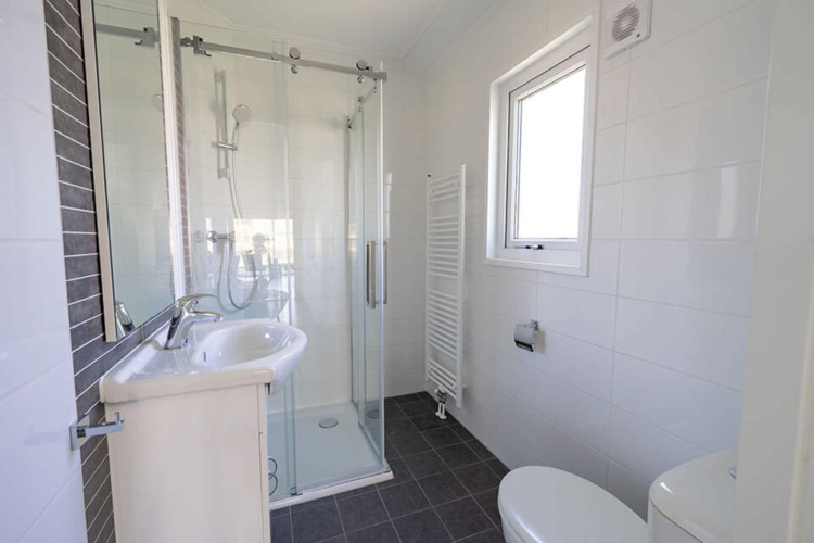 Baño moderno en la cabaña Velthorst de EuroParcs Veluwemeer, con ducha de cristal, lavabo y ventana.