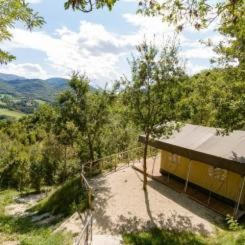 Vista di una tenda safari immersa tra alberi e colline, con montagne e cielo limpido sullo sfondo.