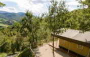 Vista di una tenda safari immersa tra alberi e colline, con montagne e cielo limpido sullo sfondo.