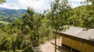 Vista di una tenda safari immersa tra alberi e colline, con montagne e cielo limpido sullo sfondo.