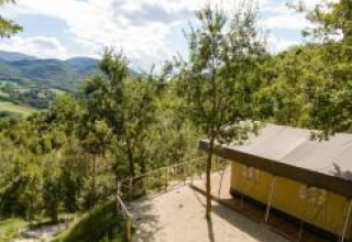 Vista de una tienda safari rodeada de árboles y colinas, con montañas y cielo despejado al fondo.