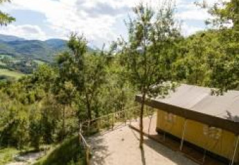 Vista di una tenda safari immersa tra alberi e colline, con montagne e cielo limpido sullo sfondo.
