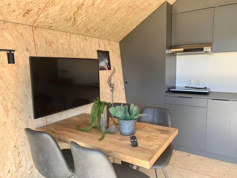 Coin repas moderne avec table en bois, chaises grises, TV et kitchenette dans la Solo Retreat à EuroParcs Veluwemeer.