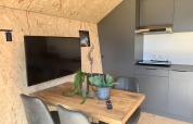 Moderne spiseplads med træbord, grå stole, tv og tekøkken i Solo Retreat-lodge ved EuroParcs Veluwemeer.