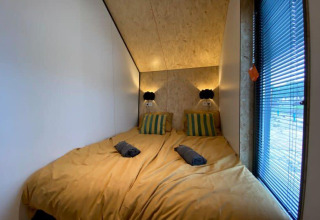 Camera con due letti, biancheria gialla e cuscini a righe al Solo Retreat presso EuroParcs Veluwemeer, Paesi Bassi.