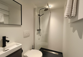 Bagno moderno e compatto con doccia, WC a muro e asciugamani al Solo Retreat di EuroParcs Veluwemeer.
