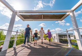 Familia cruza un puente de madera bajo el sol en Solo Retreat del EuroParcs Veluwemeer, Países Bajos.