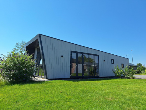 Moderne lodge Just Nature bij De Rijp in Nederland met schuine wanden, grote ramen en een groene grasmat.