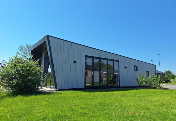 Moderne lodge Just Nature ved De Rijp i Holland, med skrå vægge, store vinduer og grøn græsplæne.