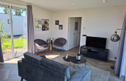 Sala moderna con sofá gris, televisor y grandes ventanales en Just Nature lodge de De Rijp, Países Bajos.
