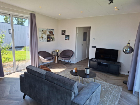 Modern lounge with gray sofa, TV, and large windows at Just Nature lodge in De Rijp, Netherlands.