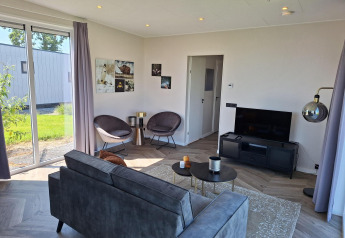 Moderne stue med store vinduer, grå sofa og fladskærms-TV i Just Nature-lodgen, De Rijp, Holland.