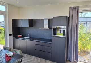 Cocina moderna en el lodge Just Nature en De Rijp, Países Bajos, con gabinetes negros y ventanas al jardín.