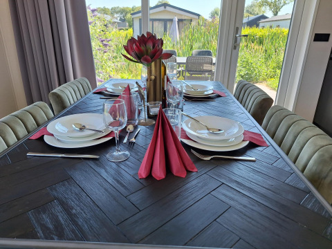 Table de salle à manger élégamment dressée avec serviettes rouges et vue sur jardin à Just Nature Lodge à De Rijp, Pays-Bas.