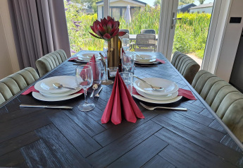 Table de salle à manger élégamment dressée avec serviettes rouges et vue sur jardin à Just Nature Lodge à De Rijp, Pays-Bas.