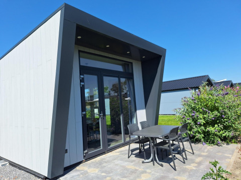 Modern lodge at Just Nature in De Rijp, Netherlands, featuring patio table, chairs, plants and clear blue sky.