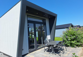 Lodge ved Just Nature i De Rijp, Holland, med moderne facade, terrassebord og stole under blå himmel.