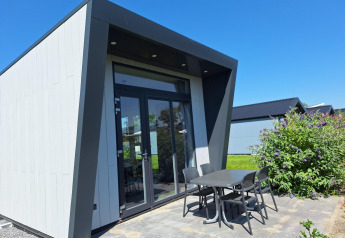 Lodge ved Just Nature i De Rijp, Holland, med moderne facade, terrassebord og stole under blå himmel.