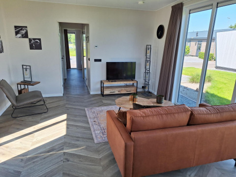 Moderne woonkamer in de Just Nature-lodge te De Rijp, Nederland, met grote ramen en een bruine zetel.