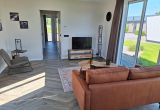 Soggiorno moderno nella lodge Just Nature a De Rijp, Paesi Bassi, con divano e grandi finestre sul verde.