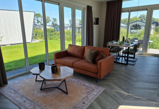 Moderne lodge Just Nature bij De Rijp in Nederland, grote ramen, een sofa en een eetruimte binnen.