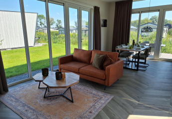 Moderne lodge Just Nature ved De Rijp i Nederlandene med store vinduer, sofa og spisebord i lyst rum.